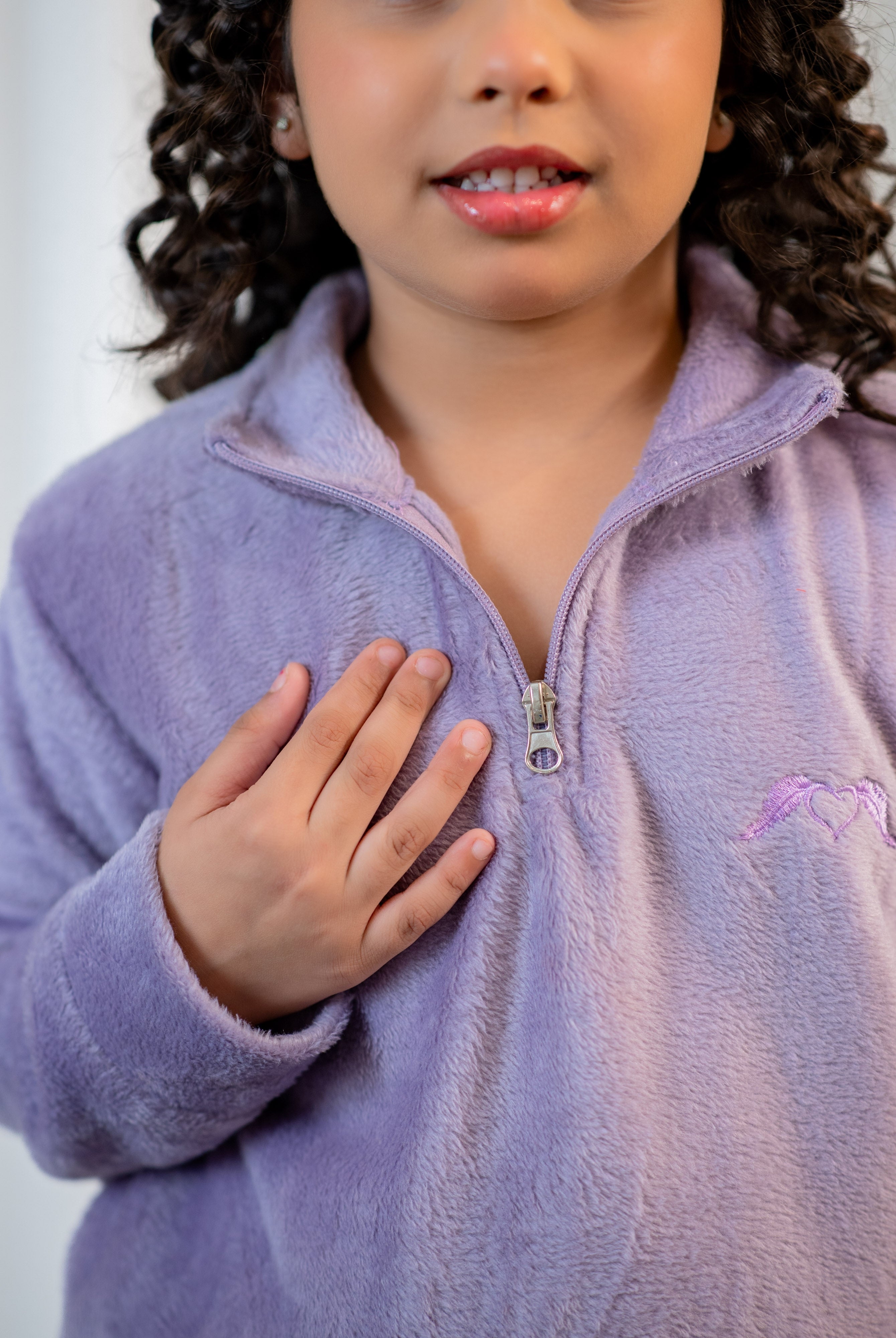 Child wearing a purple fleece jacket with a logo on a plain background