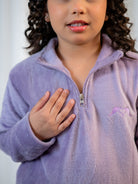 Child wearing a purple fleece jacket with a logo on a plain background